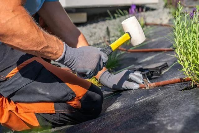 A gardener is kneeling and using a mallet to secur A gardener is kneeling and using a mallet to secur
